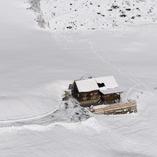 Der Hof ist ein Holzgebäude mit schneebedecktem Dach, eingebettet in eine Winterlandschaft mit Zufahrtsweg.