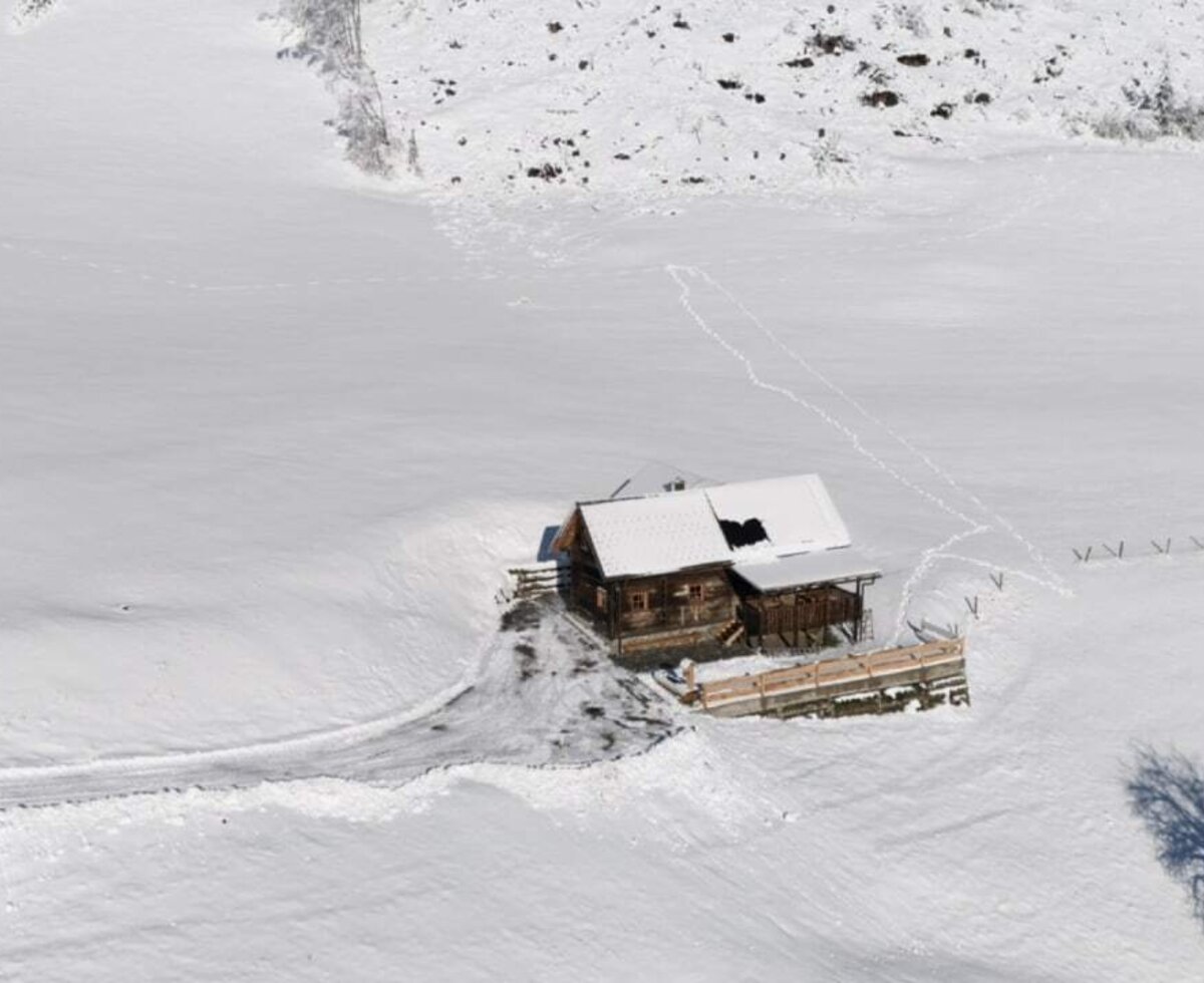 Der Hof ist ein Holzgebäude mit schneebedecktem Dach, eingebettet in eine Winterlandschaft mit Zufahrtsweg.