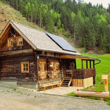 Der Hof mit traditioneller Holzfassade, überdachtem Eingangsbereich und Solarpanel auf dem Dach.