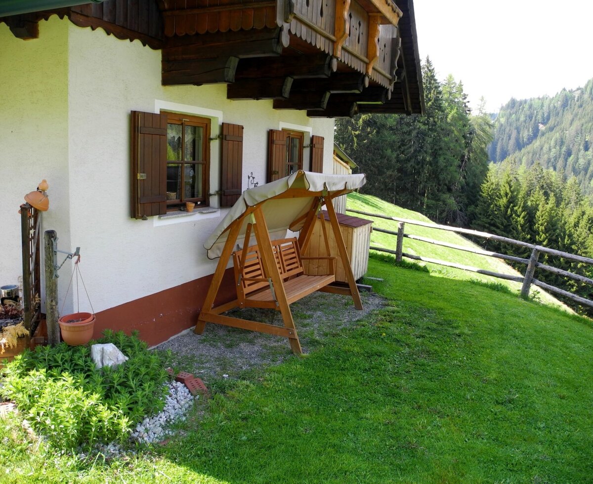 Der Sitzplatz mit Hollywoodschaukel auf der Wiese des Hofs bietet Blick auf das bewaldete Tal.