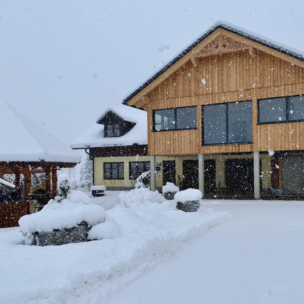 Außenansicht des Bauernhofs im Winter, mit schneebedecktem Gebäude und einem Holzpavillon.