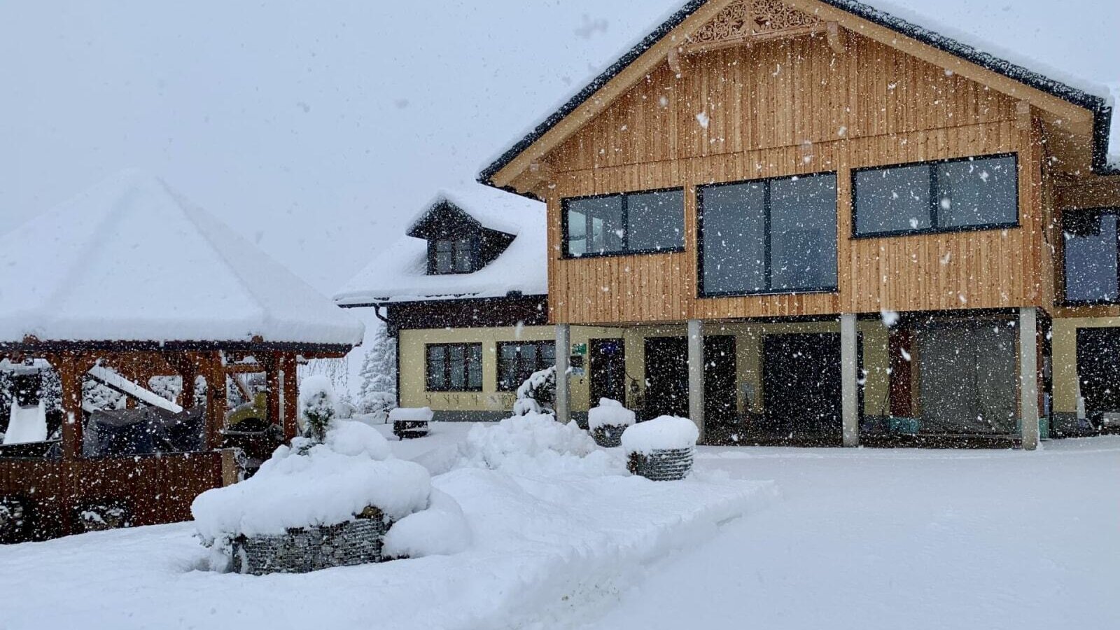 Außenansicht des Bauernhofs im Winter, mit schneebedecktem Gebäude und einem Holzpavillon.