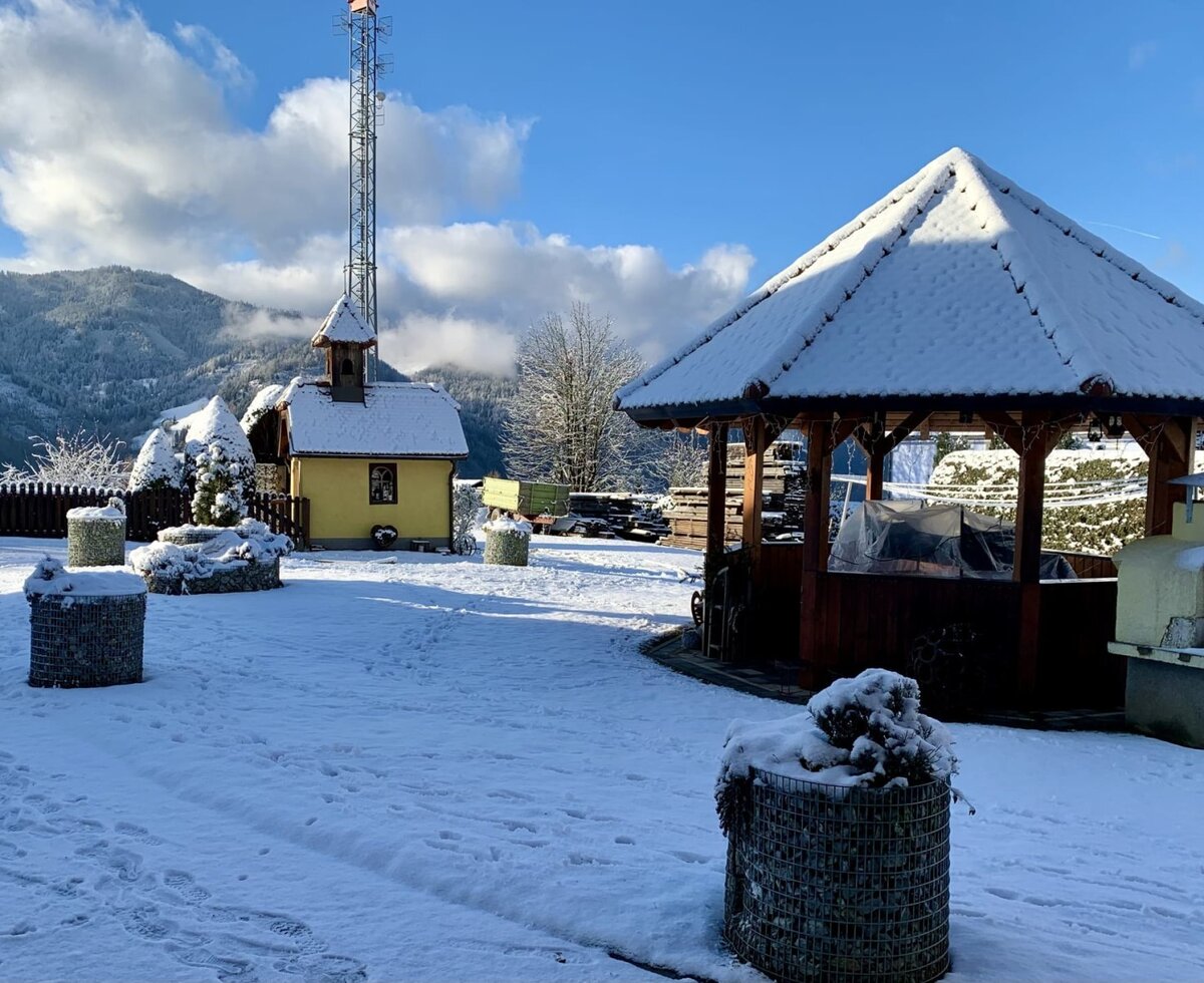 Der verschneite Außenbereich des Bauernhofs mit Pavillon, Außengrill und einer kleinen Kapelle.
