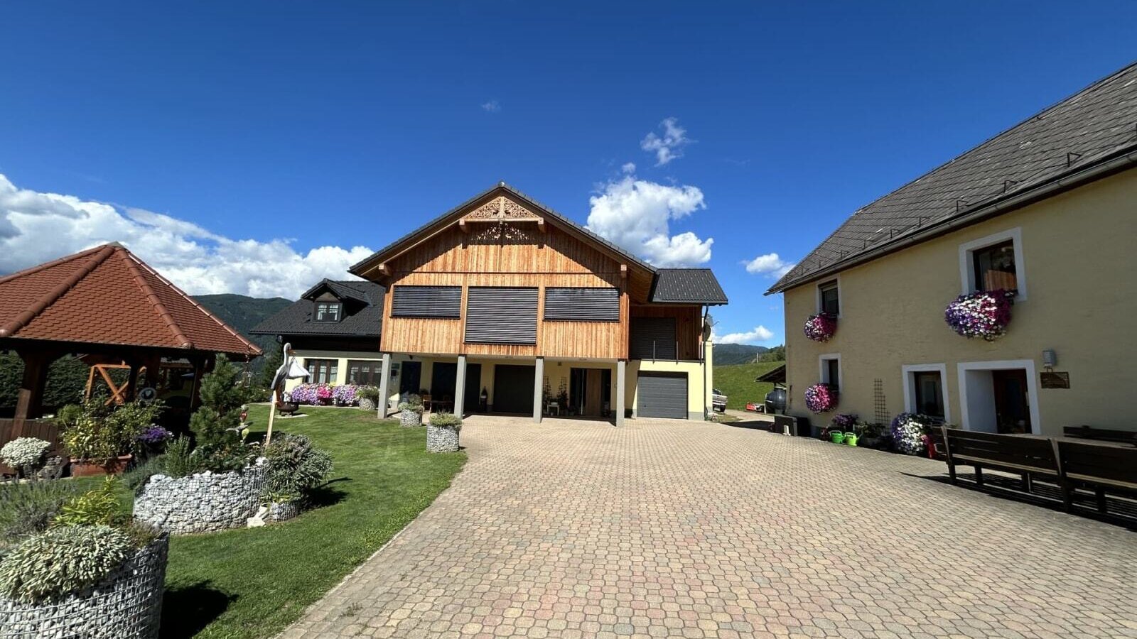 Der Außenbereich des Bauernhofs mit gepflastertem Vorplatz, den verschiedenen Gebäuden und einem Garten mit Pavillon.