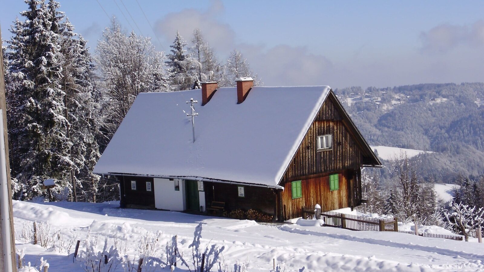 Das schneebedeckte Bauernhaus mit Holzfassade und grünen Fensterläden in der Winterlandschaft.