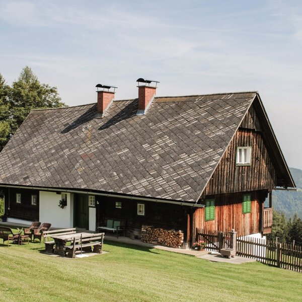 Das Bauernhaus, mit Holzfassade, einer Rasenfläche mit Sitzgelegenheiten im Freien, Kinderschaukel und Bergblick.