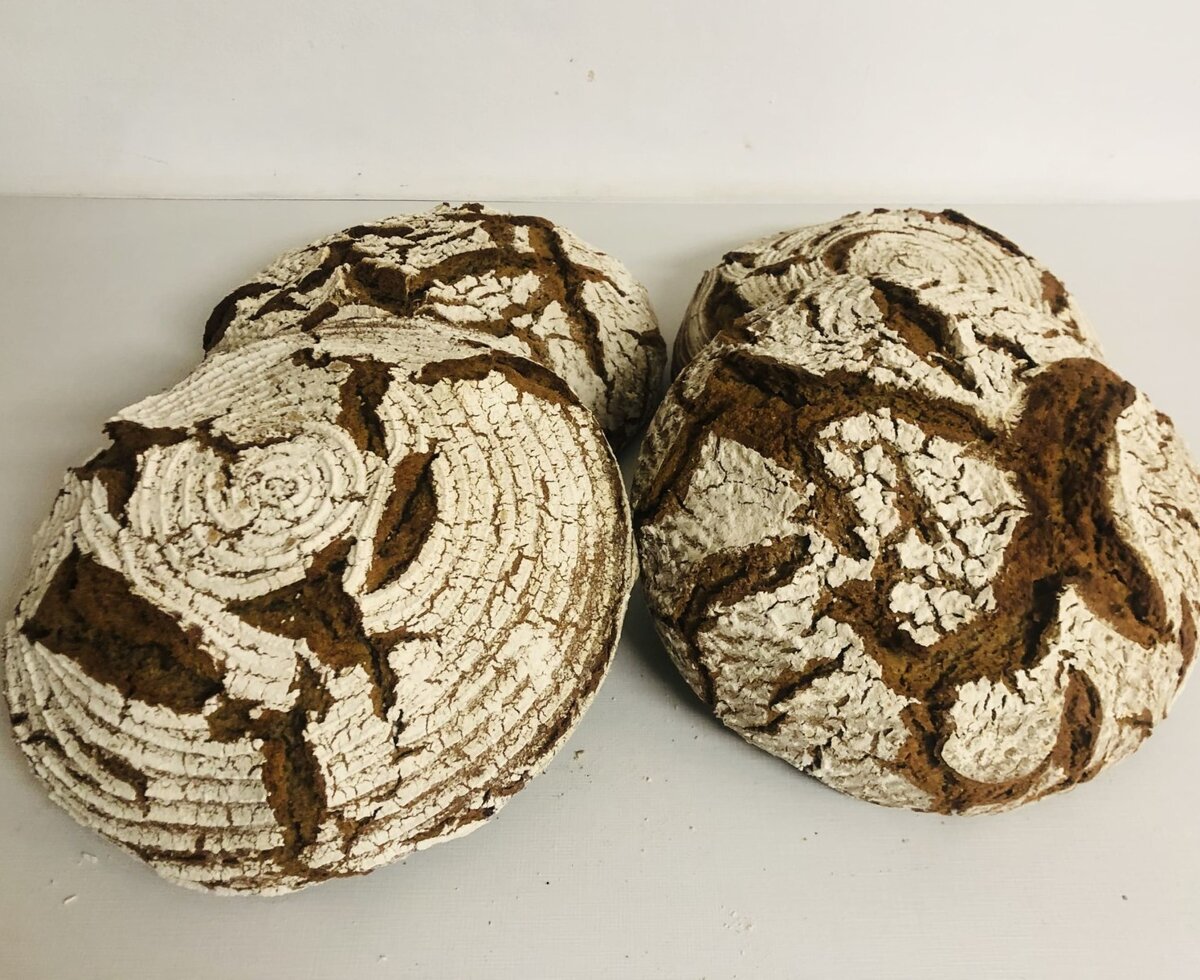 Vier Laibe rustikales Bauernbrot mit bemehlter, rissiger Kruste, als Teil des kulinarischen Angebots im Bauernhof.