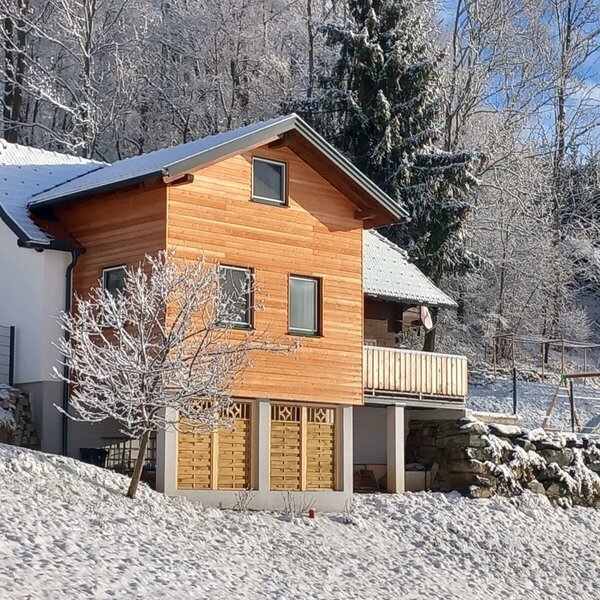 Das Ferienhaus Klampfl im Winter, umgeben von Schnee und Wald, mit einem Balkon und einem Spielbereich.