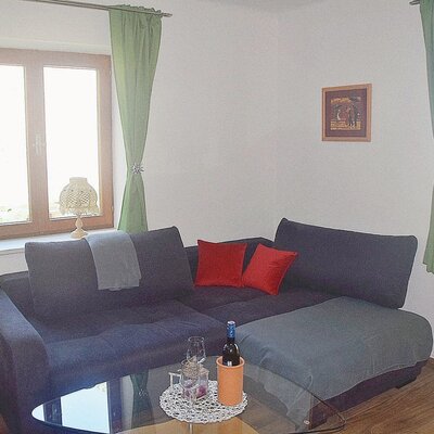 Das Wohnzimmer des Bauernhofs bietet ein L-förmiges Sofa, einen Glastisch und Fenster mit hellgrünen Vorhängen.