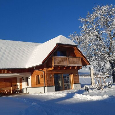 Das Ferienhaus des Bauernhofs in winterlicher Landschaft, mit Holzfassade, schneebedecktem Dach und Balkon.