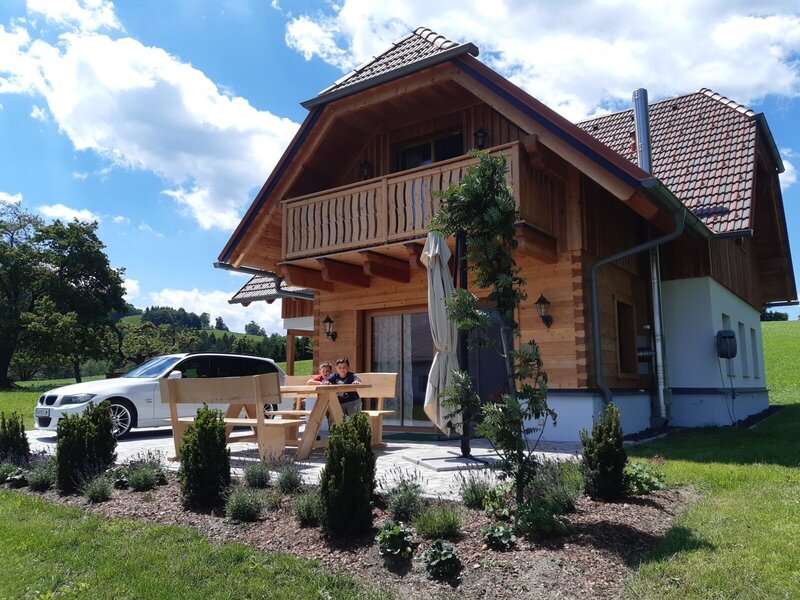 Das Ferienhaus auf dem Bauernhof mit Holzfassade, Balkon und einer Terrasse mit Holzsitzgruppe und Garten.
