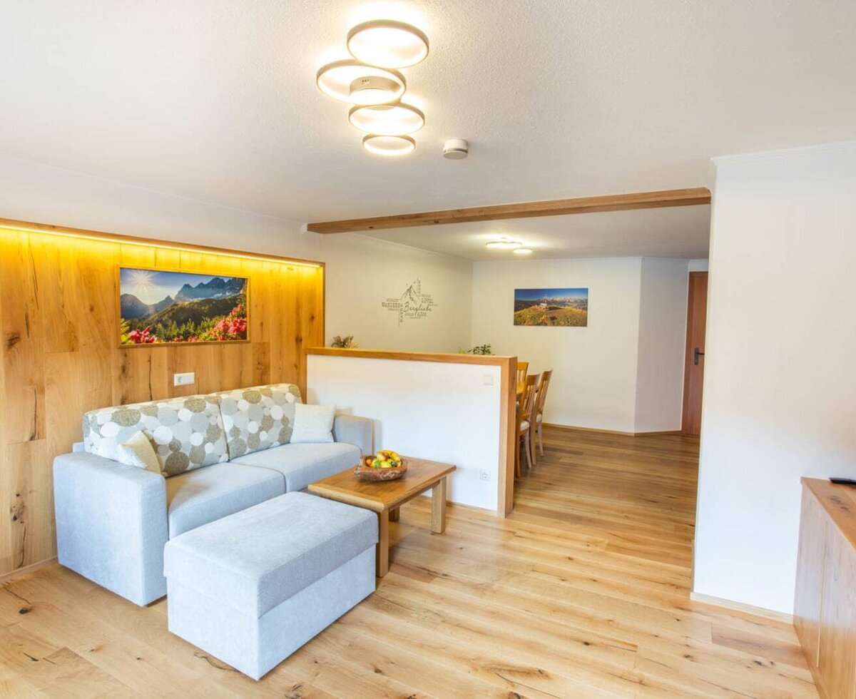 Der Wohnbereich des Appartements auf dem Bauernhof bietet ein Sofa, einen Couchtisch und eine Holzwandverkleidung mit indirekter Beleuchtung, direkt neben dem Essbereich mit Holztisch.
