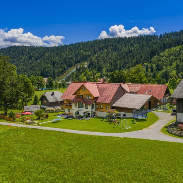 Der Bauernhof mit Spielplatz, Trampolin und Schaukeln vor einer Bergkulisse