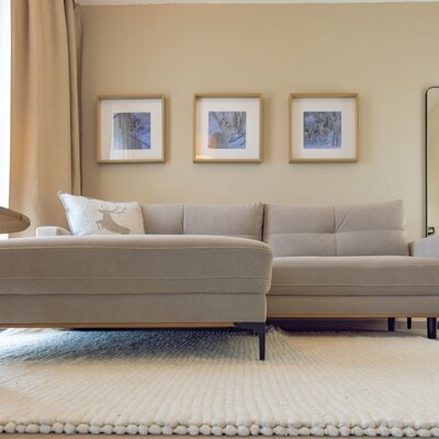 Wohnbereich mit einem L-förmigen Sofa, Wandbildern und einem Spiegel.
