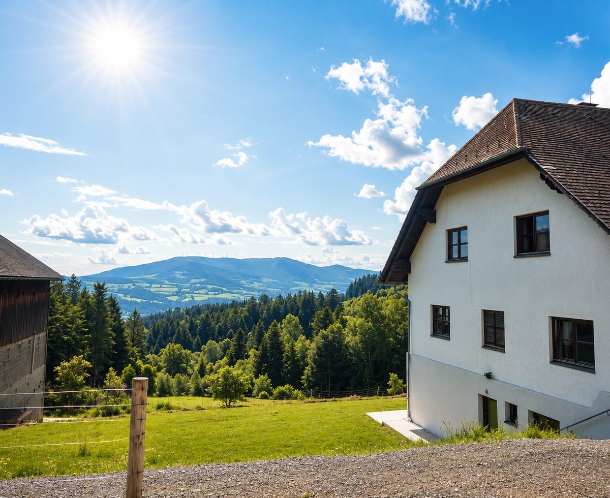 Der Bauernhof mit weißer Fassade und braunem Dach, neben einer Scheune, bietet einen weiten Blick auf grüne Wiesen, Wälder und Berge.