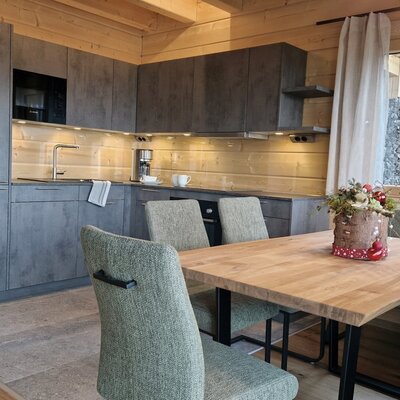 Die voll ausgestattete Küche des Bauernhofs mit modernen Schränken, Spüle, Kaffeemaschine, Herd und einem Essbereich mit Holztisch, Stühlen und Eckbank.