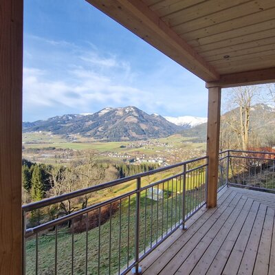 Holzbalkon des Bauernhofs mit Ausblick auf das Tal, ein Dorf und die umliegenden Berge.