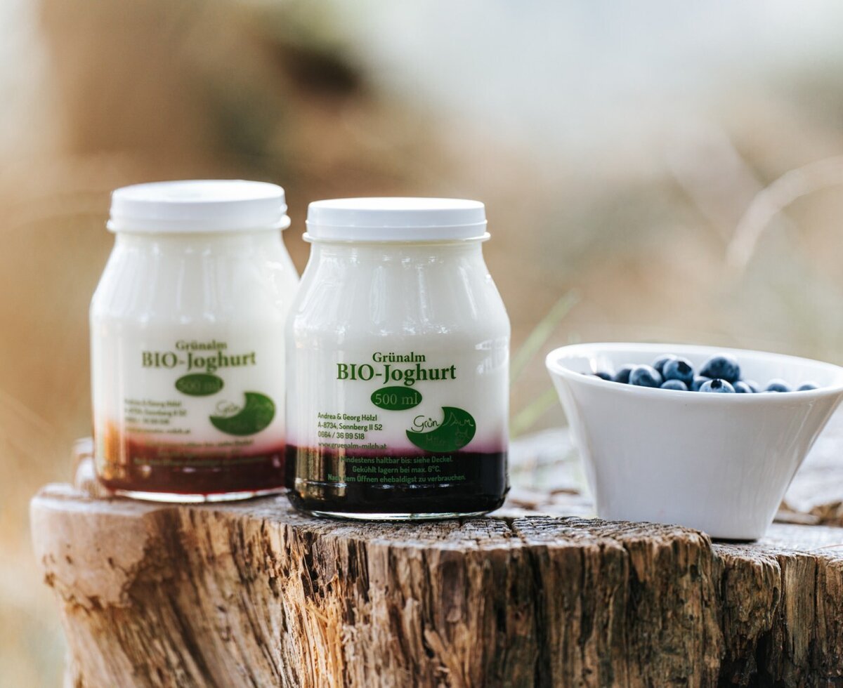 Zwei Flaschen Grünalm Bio-Joghurt und frische Heidelbeeren, die Gäste auf dem Hof genießen können.