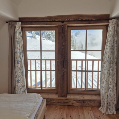 Schlafzimmer im Hof mit Holzboden und Fenstern, die einen Blick auf die winterliche Berglandschaft bieten.