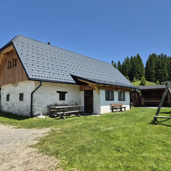 Der Hof von außen mit Grünflächen, einem überdachten Sitzplatz und einer Schaukel.