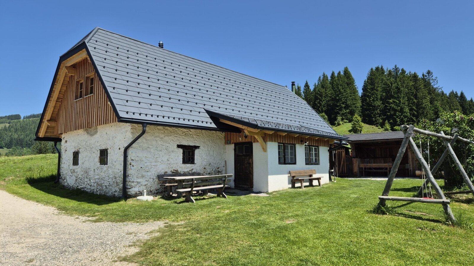 Der Hof von außen mit Grünflächen, einem überdachten Sitzplatz und einer Schaukel.