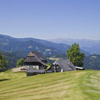 Die Almhütte und der Almstall auf einer grünen Anhöhe mit weitem Blick über die umliegende Berglandwelt.