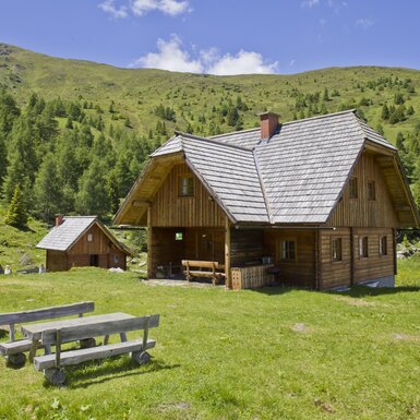Der Hof mit seinen Holzhütten und einer Grillstelle inmitten der Berglandschaft.