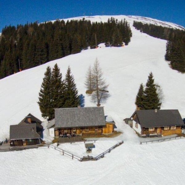 Der Hof mit seinen traditionellen Gebäuden befindet sich in einer verschneiten Berglandschaft direkt an einer Skipiste.