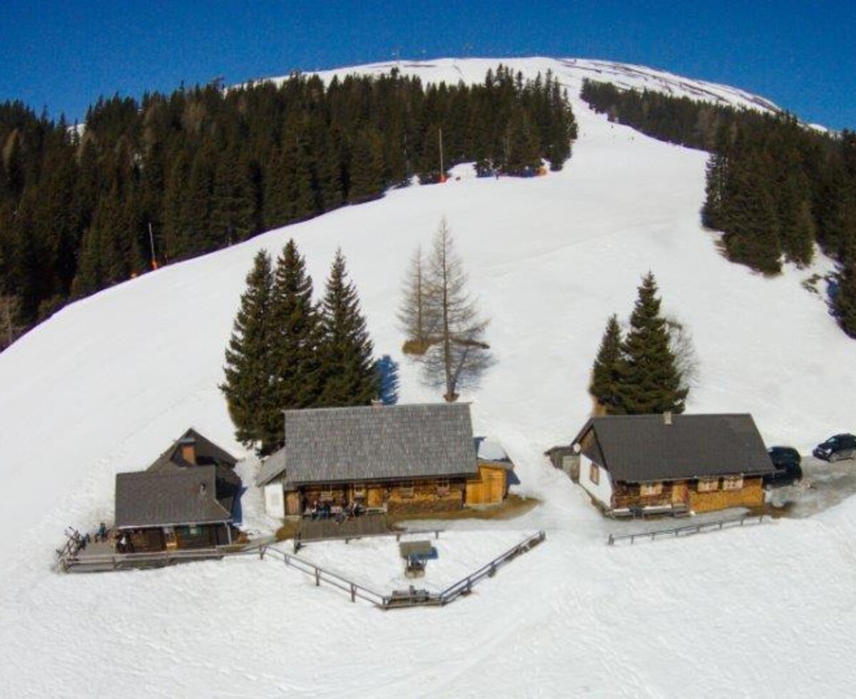Der Hof mit seinen traditionellen Gebäuden befindet sich in einer verschneiten Berglandschaft direkt an einer Skipiste.