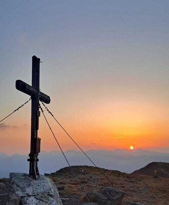 Gipfelkreuz bei Sonnenuntergang in der Berglandschaft rund um den Hof.
