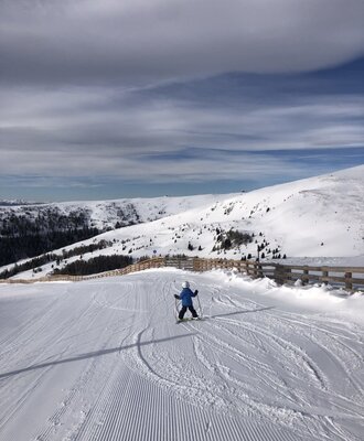 Eine Person beim Skifahren auf einer frisch präparierten Skipiste in den verschneiten Bergen.