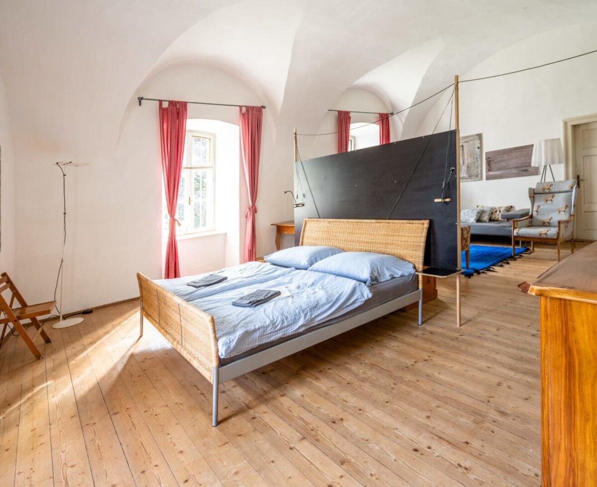 Ein geräumiges Schlafzimmer im Apartment Aurelia mit hohen Gewölbedecken, Holzböden und einem einladenden Doppelbett sowie einem angrenzenden Wohnbereich.