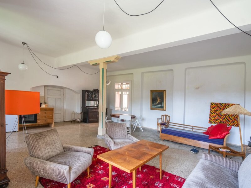 Der geräumige Wohnbereich der Ferienwohnung mit gemütlichen Retro-Sesseln, einem Holztisch und einer einladenden, künstlerischen Atmosphäre.