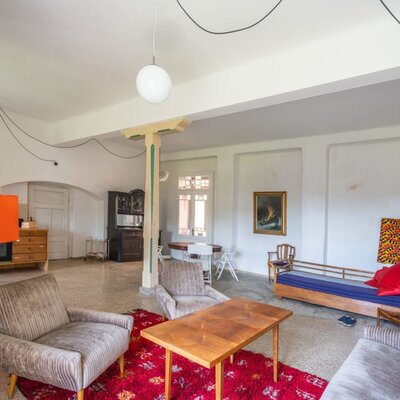 Der geräumige Wohnbereich der Ferienwohnung mit gemütlichen Retro-Sesseln, einem Holztisch und einer einladenden, künstlerischen Atmosphäre.