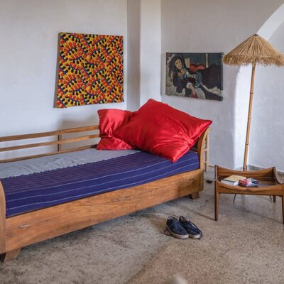 Ein gemütliches Tagesbett mit kräftigen roten Kissen und bunter Wandkunst in diesem urigen Bauernhof.