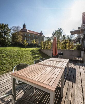 Die einladende Holzterrasse bietet einen großen Esstisch im Freien und einen schönen Blick auf das benachbarte Schloss.