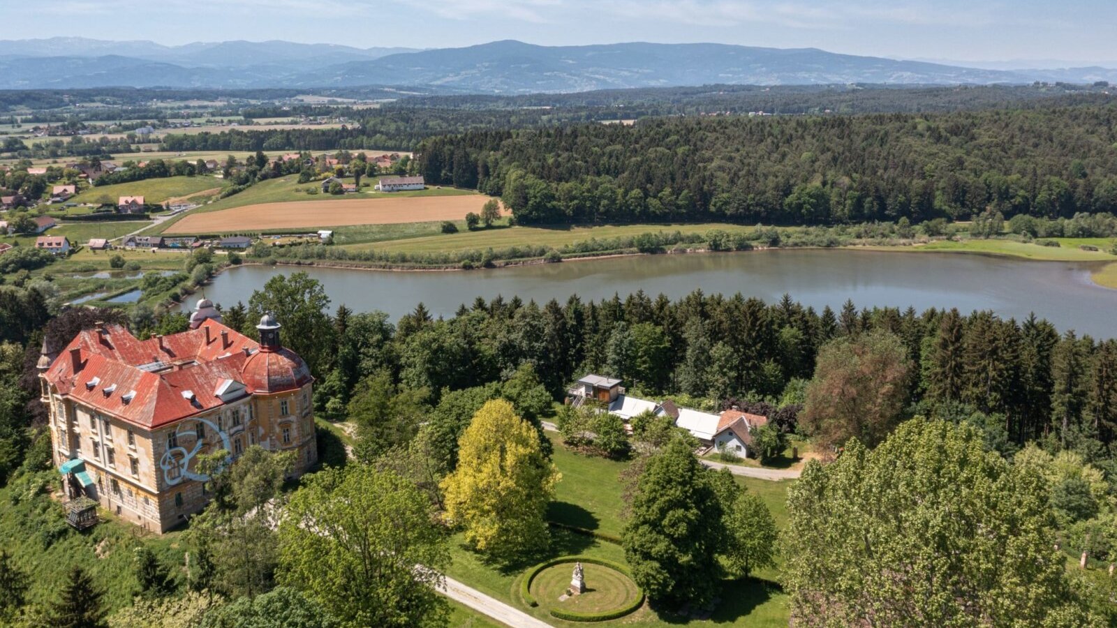 Malerische Luftaufnahme von Gut Hornegg inmitten weitläufiger grüner Felder und Wälder, mit Blick auf einen idyllischen See.