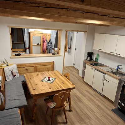 Essbereich mit Holztisch und Eckbank sowie eine Küchenzeile mit Spüle, Kochfeld und Holzofen