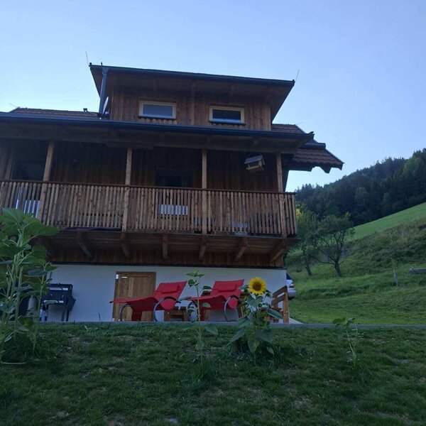 Das einladende Bed and Breakfast aus Holz mit gemütlichen roten Liegestühlen auf der Wiese vor einer grünen Hügelkulisse.