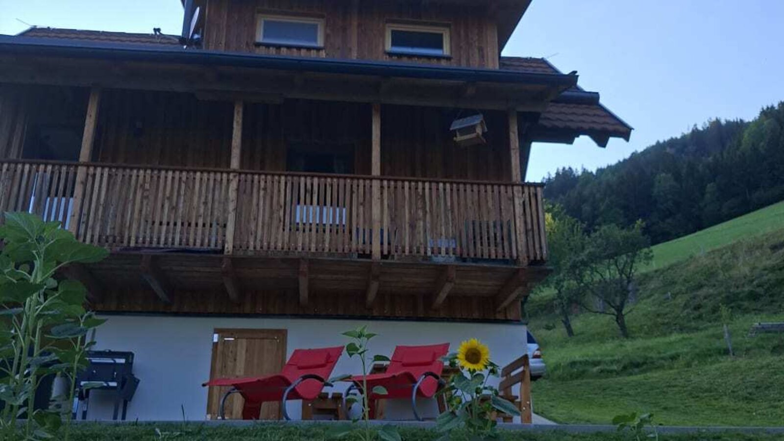Das einladende Bed and Breakfast aus Holz mit gemütlichen roten Liegestühlen auf der Wiese vor einer grünen Hügelkulisse.