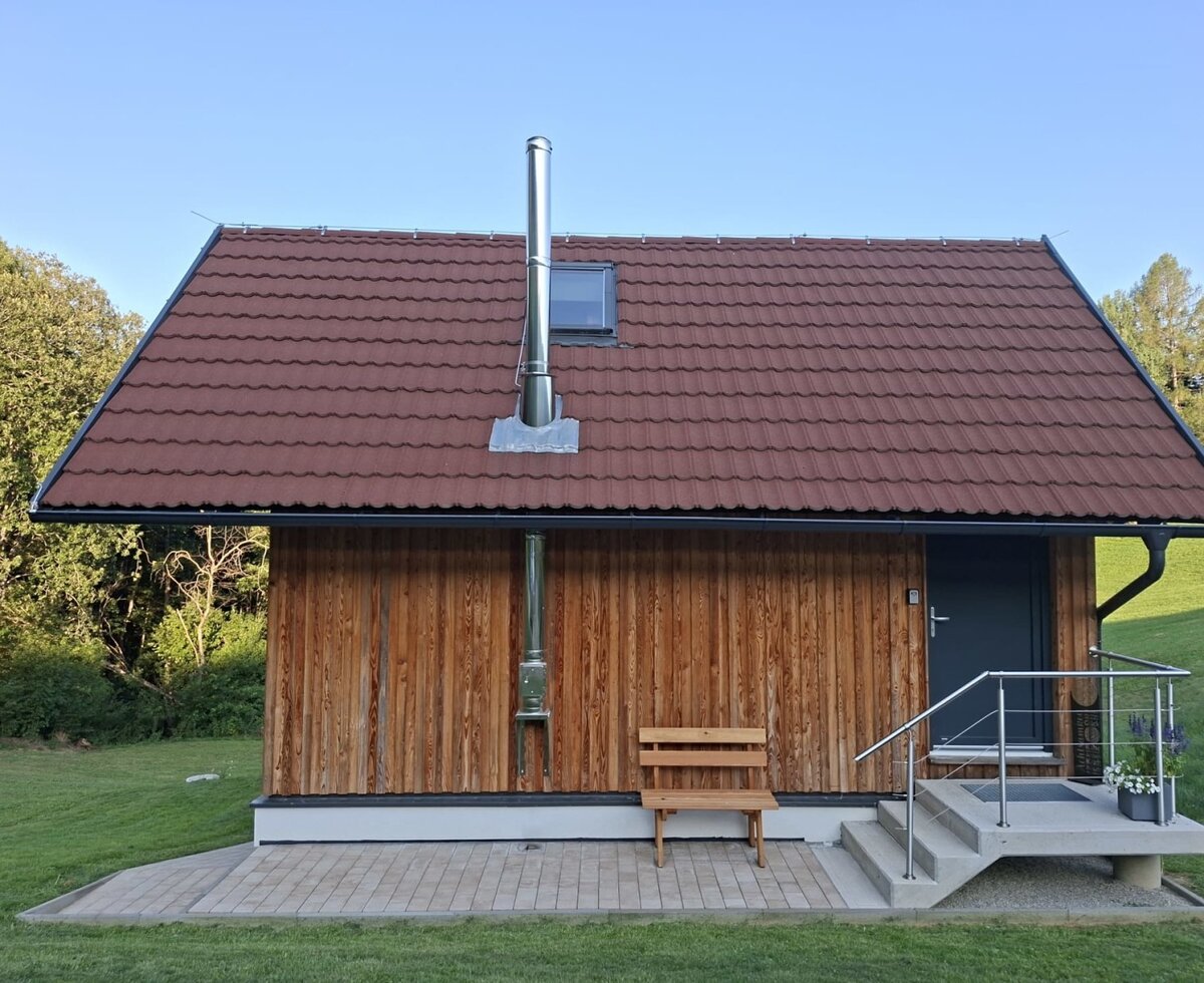 Die charmante Außenansicht des Bed and Breakfasts mit seiner warmen Holzfassade, einer gemütlichen Holzbank und einer einladenden Grünfläche.