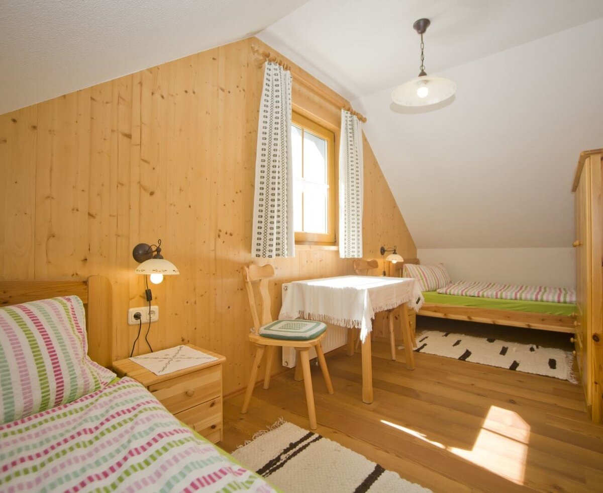 Schlafzimmer in der Almhütte mit zwei Einzelbetten, Holztäfelung, Fenster, einem Tisch mit Stühlen und einem Kleiderschrank.