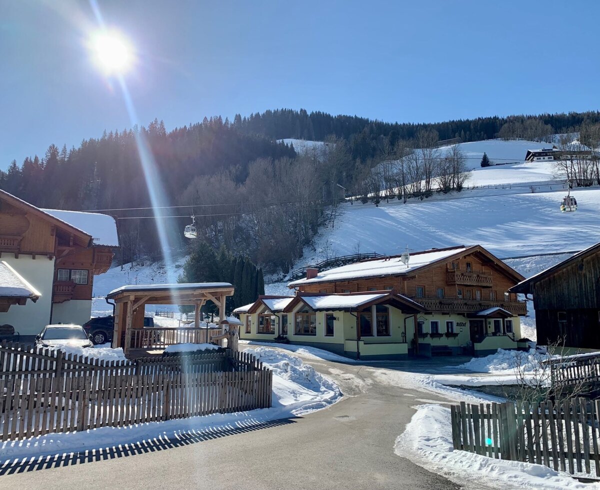 Außenansicht des Bauernhofs im Winter, umgeben von verschneiten Bergen und der Hochwurzenbahn im Hintergrund