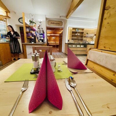 Ein gedeckter Tisch im Essbereich, mit Besteck und Servietten, im Hintergrund sind ein Buffet