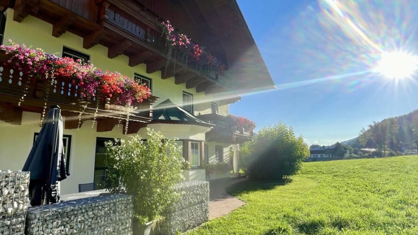 Außenansicht des Landhauses mit blumengeschmückten Balkonen und angrenzender grüner Wiese.