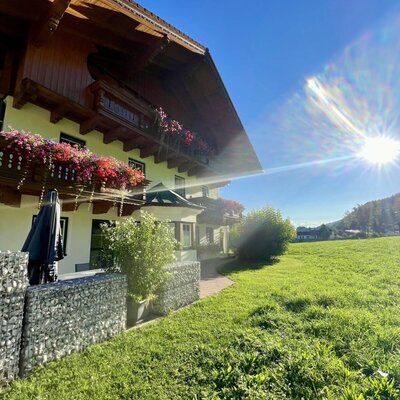 Außenansicht des Landhauses mit blumengeschmückten Balkonen und angrenzender grüner Wiese.