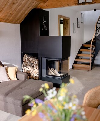 Der Holzkamin mit gestapeltem Brennholz, ein Sofa und die Treppe im Wohnbereich des Bauernhofs.