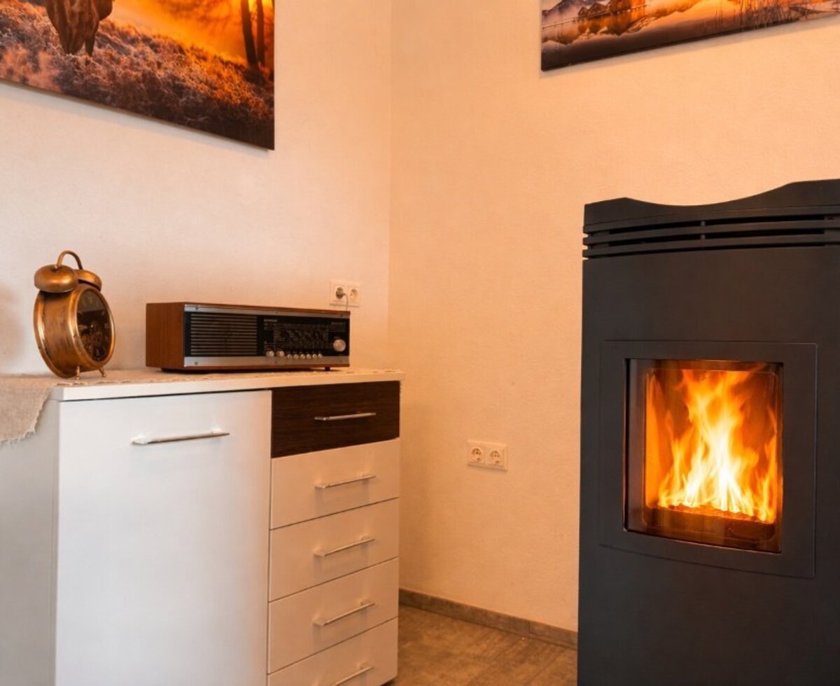 Der Kaminofen mit brennendem Feuer im Bed and Breakfast, daneben eine Kommode mit Wecker und Radio.