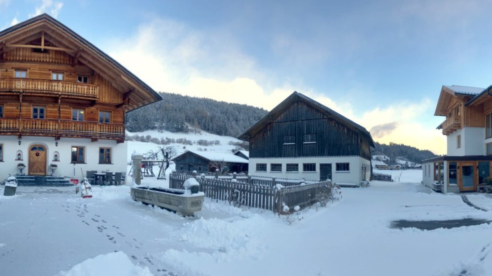Die schneebedeckte Außenansicht des Bauernhofs mit seinen Gebäuden und der winterlichen Berglandschaft.