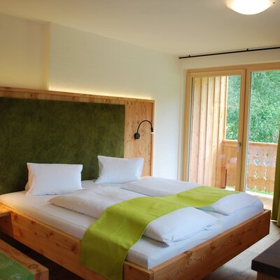 Doppelzimmer im Bauernhof mit Holzbett, grüner Kopfstütze, Leselampen und Balkonzugang.
